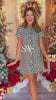 This mini dress features an all-over black and white houndstooth print, vintage-inspired pearlized buttons, and a flattering tailored silhouette that makes it perfect for holiday parties, winter events, and festive gatherings. Crafted with a cozy woven fabric, this short-sleeve dress balances elegance and comfort with front pockets and a slightly A-line shape. Whether you're headed to a Christmas brunch or a winter cocktail party, this houndstooth mini dress is your go-to seasonal staple.